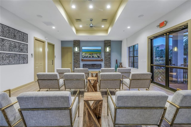 cinema room with ceiling fan, light hardwood / wood-style floors, a fireplace, and a tray ceiling