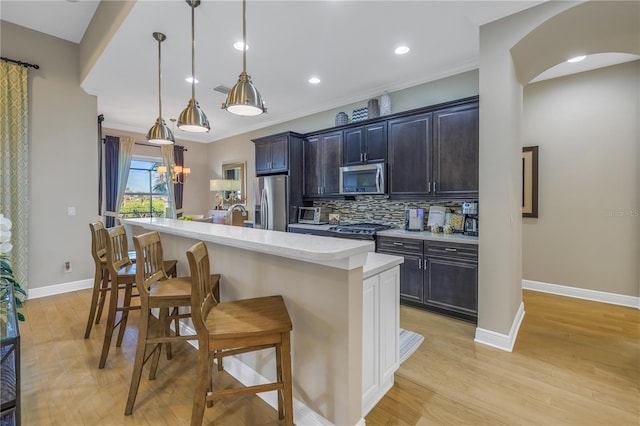 kitchen with a kitchen breakfast bar, tasteful backsplash, stainless steel appliances, a kitchen island with sink, and decorative light fixtures