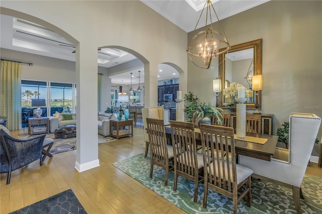 dining room with an inviting chandelier, a towering ceiling, and light hardwood / wood-style flooring