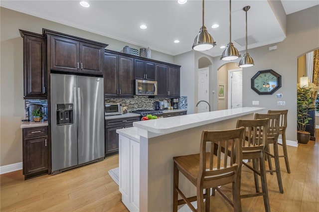 kitchen with dark brown cabinetry, an island with sink, pendant lighting, a breakfast bar, and appliances with stainless steel finishes