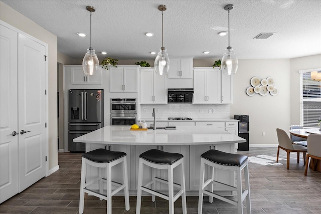 kitchen with white cabinets, a center island with sink, sink, appliances with stainless steel finishes, and wood-type flooring