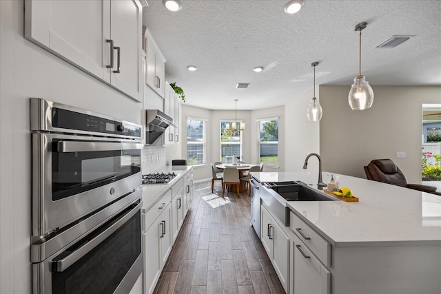 kitchen featuring appliances with stainless steel finishes, dark hardwood / wood-style flooring, white cabinetry, hanging light fixtures, and an island with sink