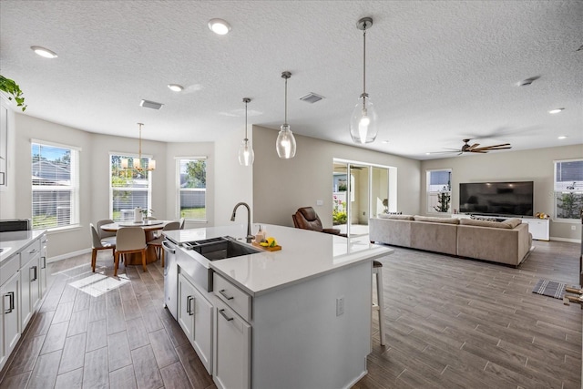 kitchen with pendant lighting, white cabinets, sink, an island with sink, and dark hardwood / wood-style flooring