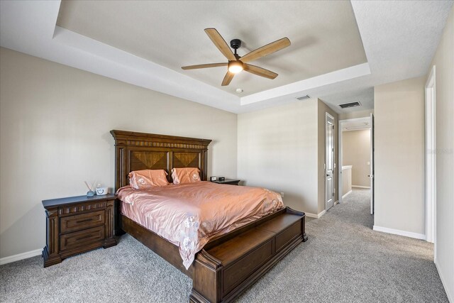 carpeted bedroom with ceiling fan and a raised ceiling