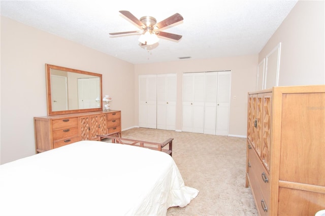 bedroom with two closets, ceiling fan, light colored carpet, and a textured ceiling