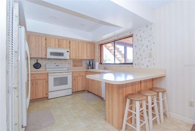 kitchen featuring white appliances, a kitchen breakfast bar, sink, tasteful backsplash, and kitchen peninsula