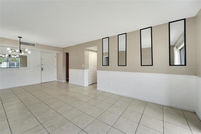 tiled spare room with a notable chandelier