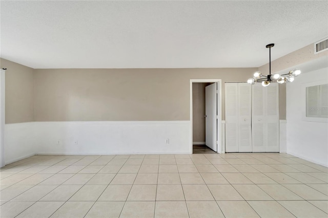 spare room featuring a chandelier, light tile patterned floors, and a textured ceiling