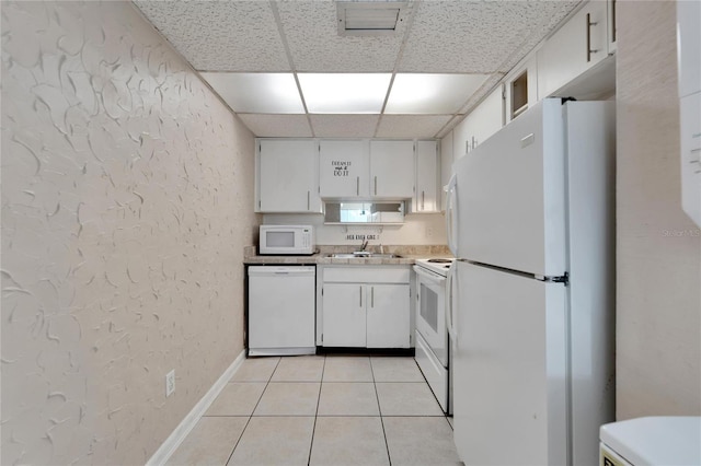 kitchen with a paneled ceiling, white appliances, white cabinets, sink, and light tile patterned floors