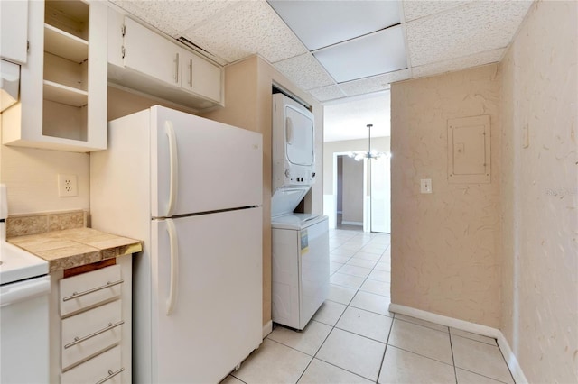 kitchen with a paneled ceiling, white appliances, hanging light fixtures, stacked washing maching and dryer, and light tile patterned floors