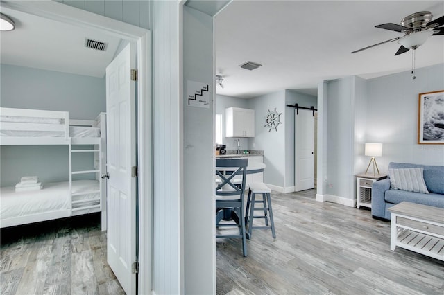 12321 Gulf Blvd, Treasure Island, FL 33706 - bedroom with a barn door, light wood-type flooring, baseboards, and a ceiling fan