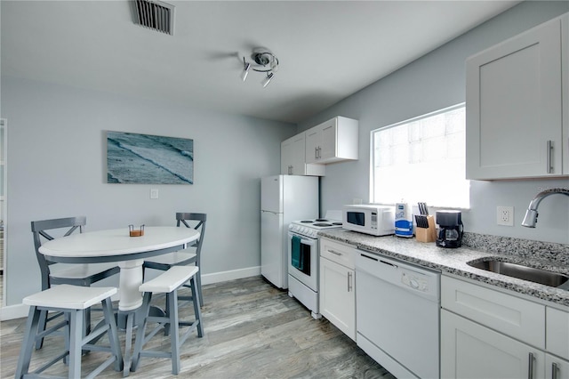 12321 Gulf Blvd, Treasure Island, FL 33706 - kitchen featuring white appliances, a sink, light wood-style flooring, light stone countertops, and white cabinetry