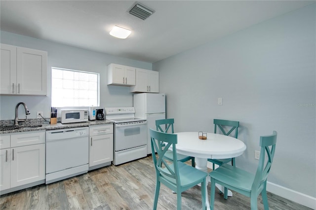 12321 Gulf Blvd, Treasure Island, FL 33706 - kitchen with white appliances, a sink, light wood-style floors, light stone countertops, and white cabinets