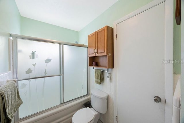 bathroom with shower / bath combination with glass door, toilet, and tile walls