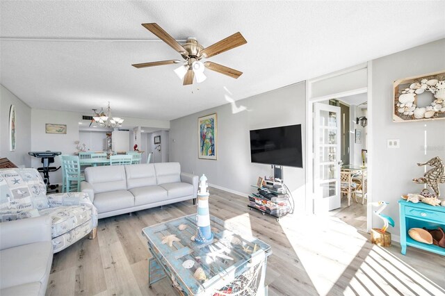 living room with ceiling fan with notable chandelier, light hardwood / wood-style floors, and a textured ceiling