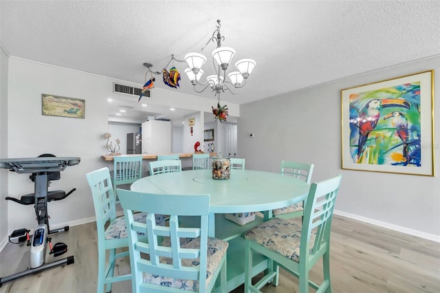 dining area with a textured ceiling, light hardwood / wood-style flooring, and a notable chandelier