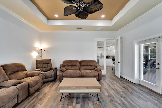 living room with ceiling fan, a raised ceiling, wood-type flooring, and ornamental molding