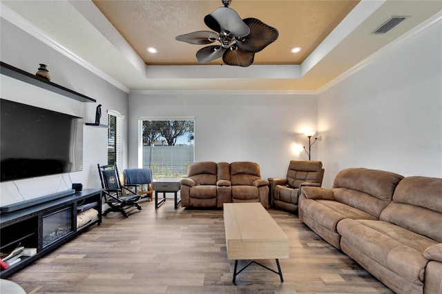 living room featuring a tray ceiling, light hardwood / wood-style flooring, and ornamental molding