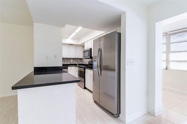 kitchen featuring kitchen peninsula, appliances with stainless steel finishes, tasteful backsplash, light tile patterned floors, and white cabinetry