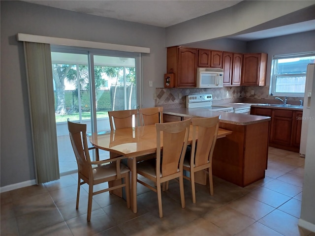 kitchen featuring tasteful backsplash, sink, light tile patterned floors, kitchen peninsula, and white appliances