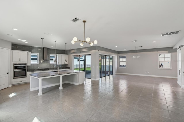 kitchen featuring light tile patterned floors, a center island with sink, white cabinetry, and a wealth of natural light