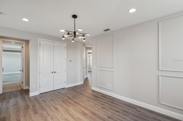 unfurnished bedroom featuring hardwood / wood-style floors, an inviting chandelier, and a closet