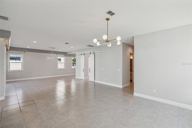 empty room with a barn door, plenty of natural light, light tile patterned floors, and an inviting chandelier