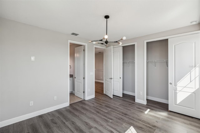 unfurnished bedroom with hardwood / wood-style flooring, multiple closets, and a notable chandelier