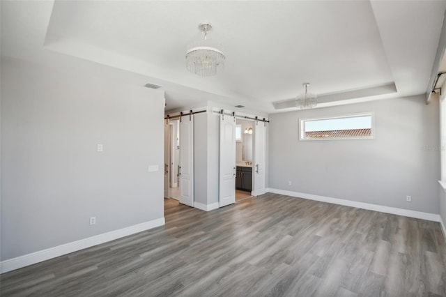 unfurnished bedroom featuring wood-type flooring, a barn door, a tray ceiling, and ensuite bathroom