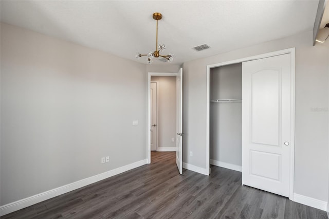 unfurnished bedroom featuring a closet, dark wood-type flooring, and a notable chandelier