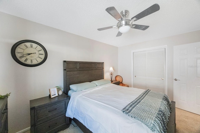 bedroom featuring ceiling fan, a closet, light colored carpet, and a textured ceiling