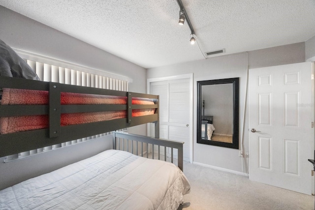 bedroom with a textured ceiling, a closet, light colored carpet, and track lighting