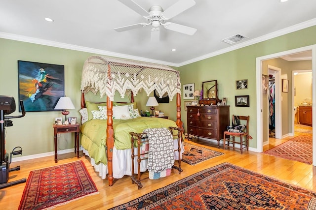 bedroom with a walk in closet, ceiling fan, wood-type flooring, and ornamental molding