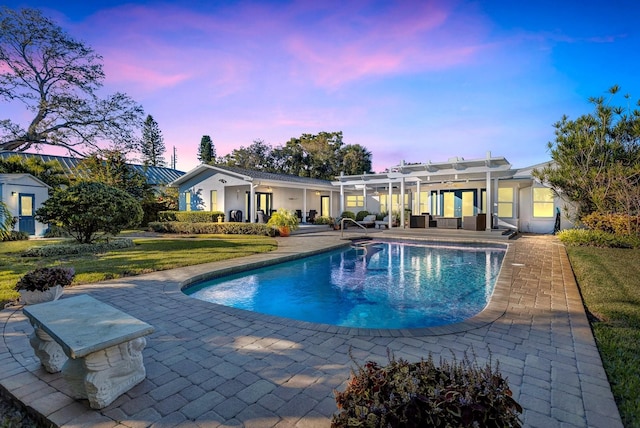 pool at dusk featuring a pergola, a lawn, and a patio