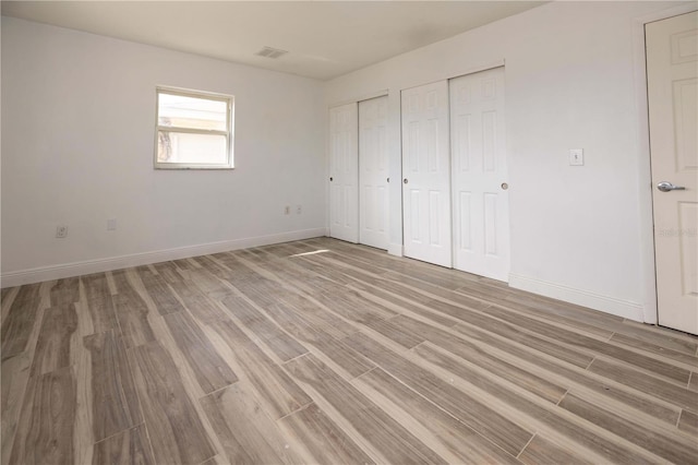 unfurnished bedroom with two closets and light hardwood / wood-style flooring