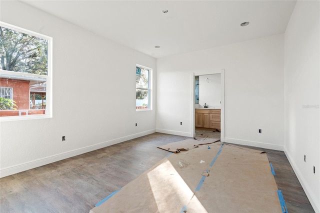 unfurnished bedroom featuring multiple windows, sink, hardwood / wood-style flooring, and ensuite bathroom