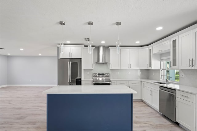 kitchen with light wood-style flooring, appliances with stainless steel finishes, a sink, a center island, and wall chimney exhaust hood