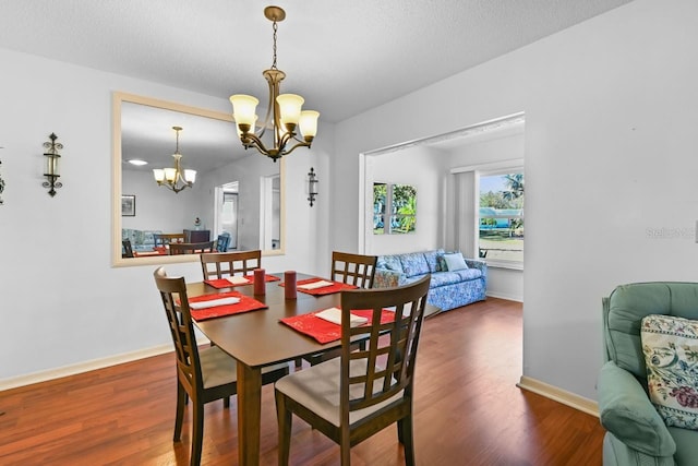 dining area with dark wood-type flooring, a textured ceiling, and an inviting chandelier