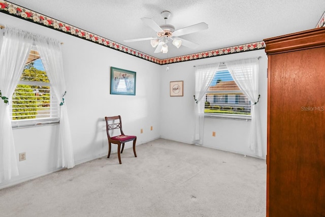 living area featuring a textured ceiling, light colored carpet, and ceiling fan