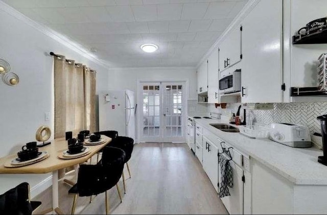 kitchen featuring white appliances, white cabinets, crown molding, sink, and light wood-type flooring