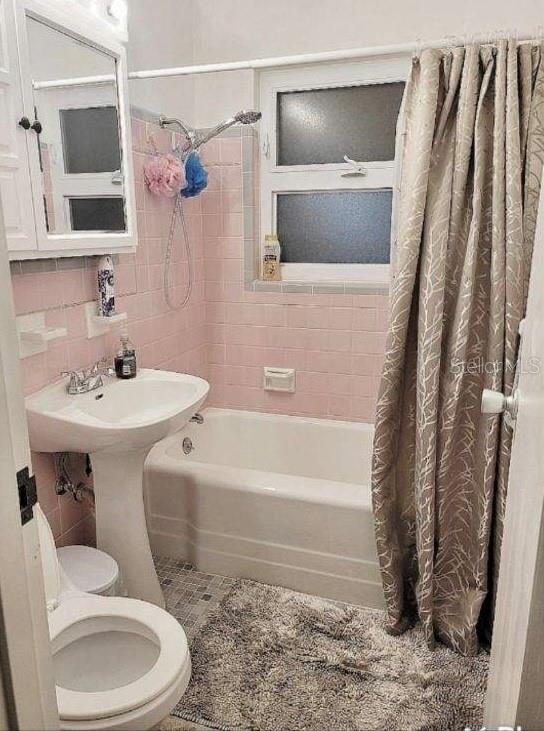 bathroom with tile patterned flooring, decorative backsplash, toilet, tile walls, and shower / tub combo with curtain