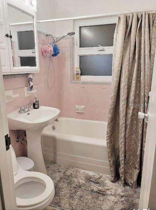 bathroom with tasteful backsplash, tile walls, toilet, and shower / tub combo with curtain