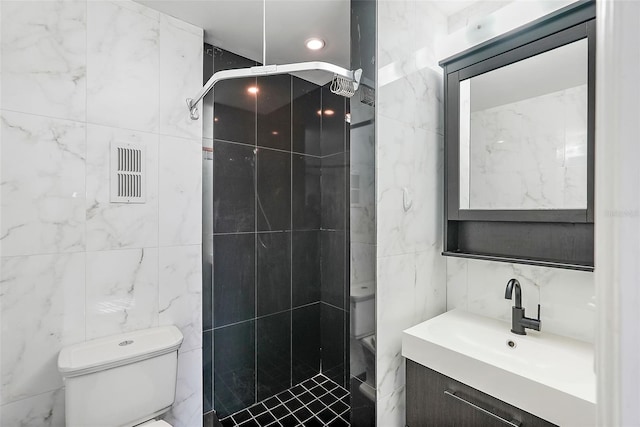 bathroom with a tile shower, vanity, tile walls, and toilet