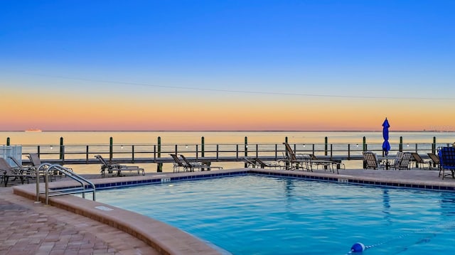 pool at dusk featuring a patio area and a water view