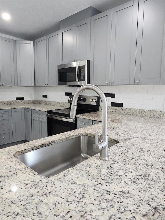 kitchen with gray cabinets, light stone countertops, and appliances with stainless steel finishes