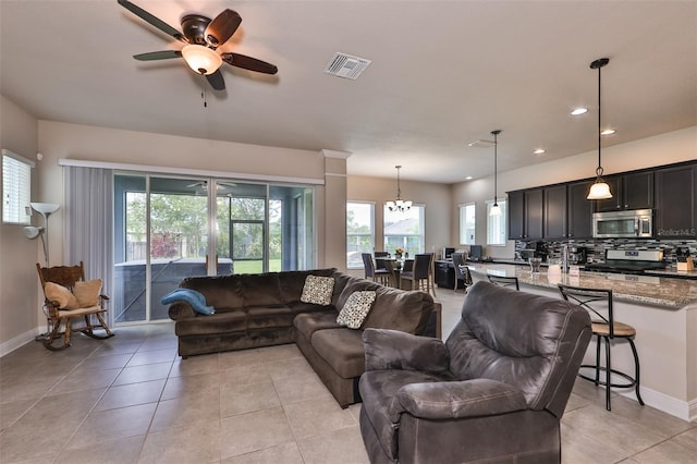 living room with plenty of natural light, light tile patterned floors, and ceiling fan with notable chandelier