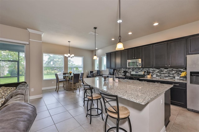 kitchen featuring light stone countertops, stainless steel appliances, backsplash, an island with sink, and pendant lighting