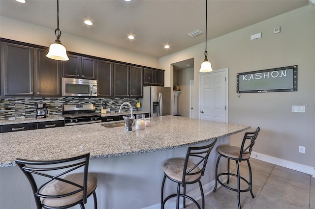 kitchen with decorative light fixtures, sink, stainless steel appliances, and an island with sink