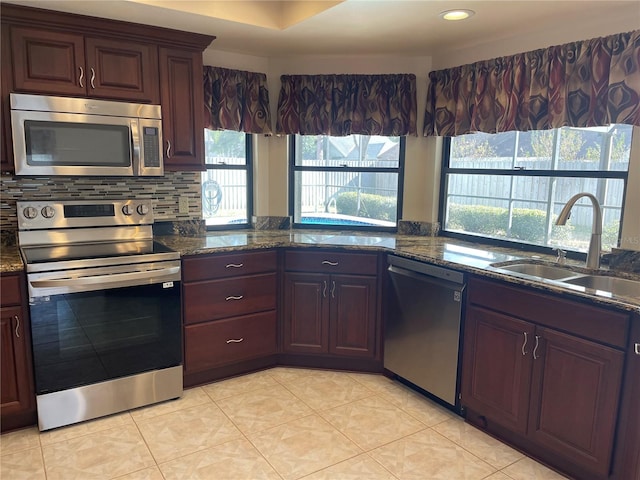 kitchen with backsplash, stainless steel appliances, sink, light tile patterned floors, and dark stone countertops