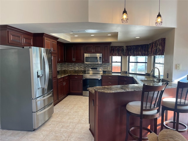 kitchen with sink, stainless steel appliances, a tray ceiling, decorative light fixtures, and kitchen peninsula